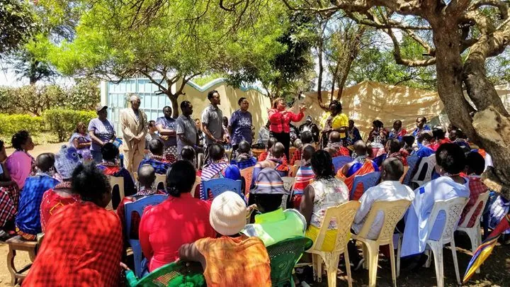 A community gathering seated outdoors under trees